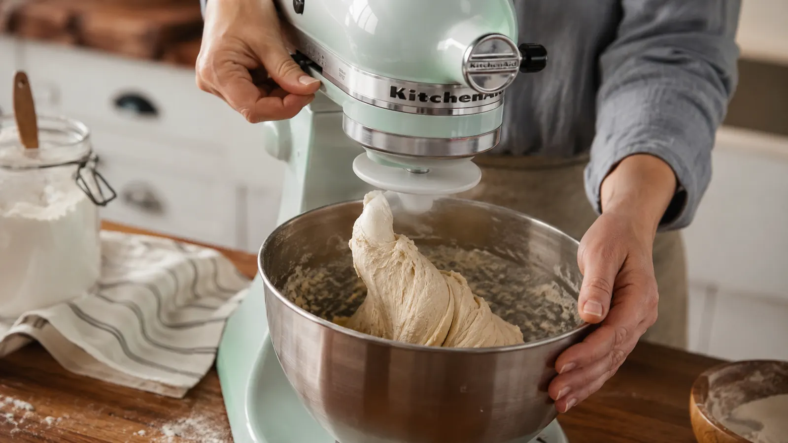 Dough hook attachment on stand mixer kneading shaggy bread dough in a stainless steel mixing bowl